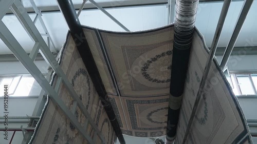 Large patterned carpets hanging from industrial metal racks during the manufacturing process in a factory.