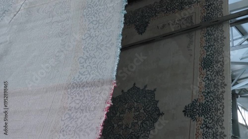 Detailed close up of traditional floral carpet patterns hanging in a large textile manufacturing facility.