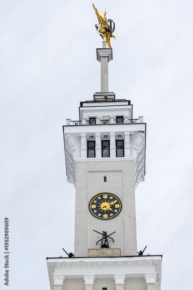 Fototapeta premium Front view of historic clock tower topped by a Soviet golden star rises against a cloudy sky. The North River Terminal or Rechnoy Vokzal of Moscow, Russia. It was built in 1937