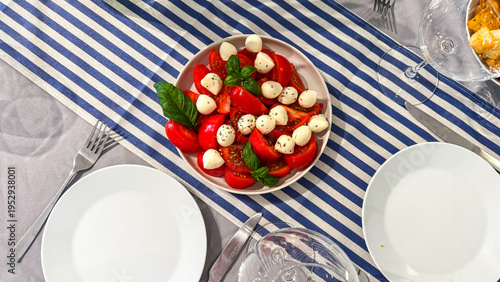 Top-down Caprese salad on a blue-striped tablecloth in bright natural summer light, evoking casual alfresco dining  suitable for food blogs, menus, lifestyle and social media