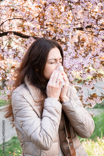 Vertical shot of a woman blowing her nose outdoors. Spring allergy symptom, hay fever relief, seasonal cold.