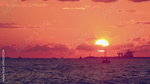 Number 4. Dramatic red-orange sunset, with the outline of coastline and ships and sailboats floating on water visible on horizon. Not AI