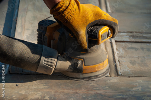 Photography A close-up of a gloved hand operating a palm sander on an old wooden door