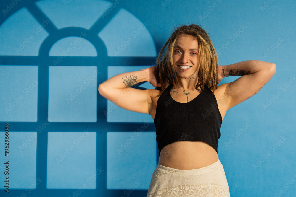 Fototapeta premium Confident woman with dreadlocks smiling against blue wall