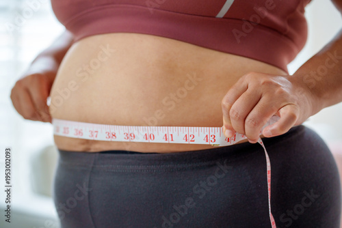 Determined woman checking waist size with measuring tape, Health care and obesity control concept.