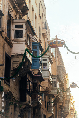Buildings with typical Maltese balconies (gallarijas) in shade and sunlight, garlands with hanging crowns, Valletta MALTA