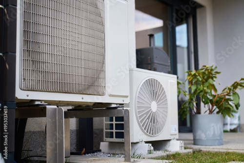 Outdoor heat pump units installed beside modern house on patio and grass. Concept of residential heating, cooling, energy efficiency and home technology
