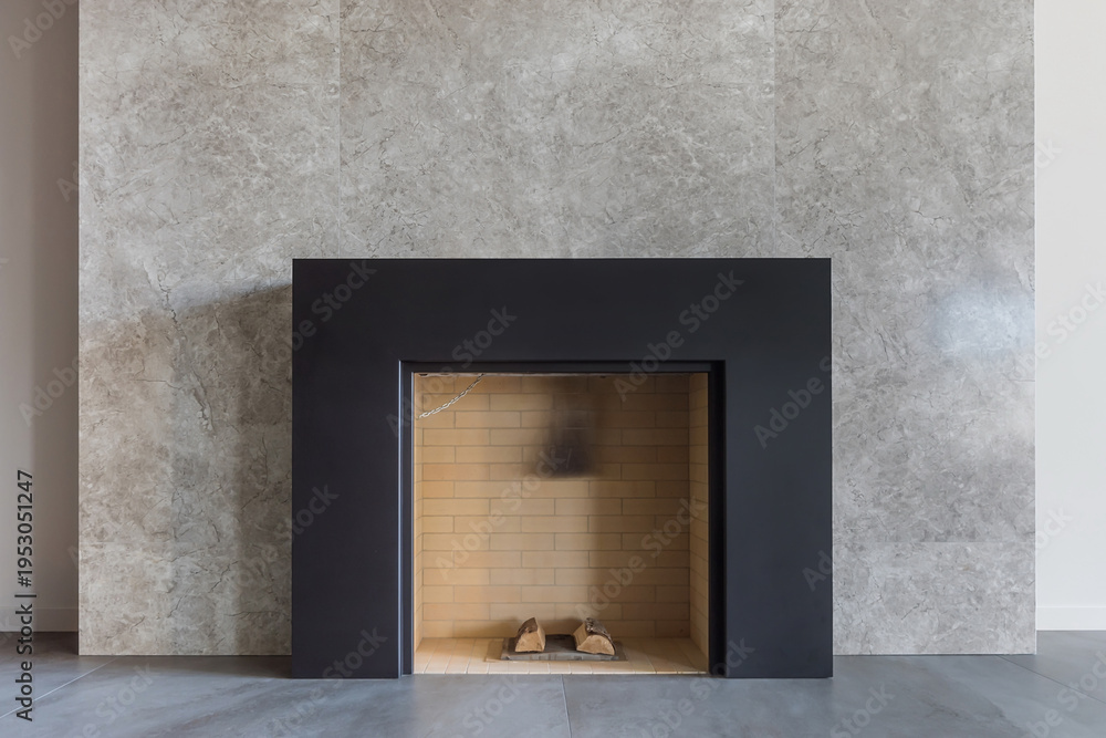 Obraz premium A fireplace is placed in a minimalist living room with a stone wall. The space is bright with natural light. The design is simple and clean. A few logs rest inside the fireplace