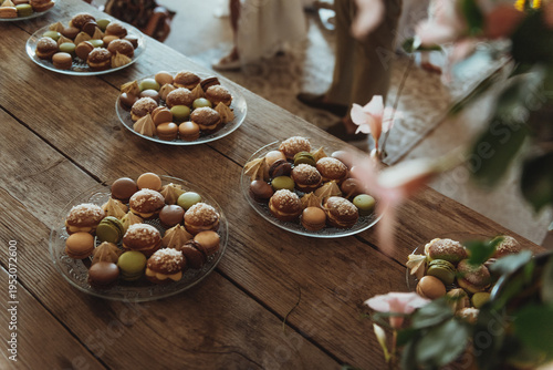 Sweets, small bites like chocolate and cookies served on plates on a wooden table during a party inside a restaurant framed by blooming flowers.