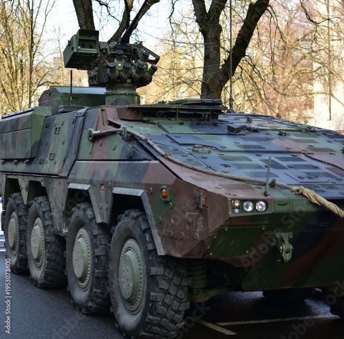 Slika na platnu Close view of a modern camouflaged armored vehicle with weapon station and multiple wheels, parked outdoors on a wet urban street in daylight