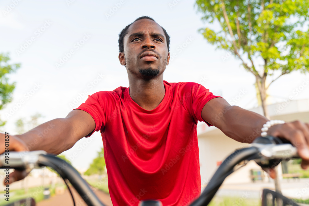 Obraz premium Young man sitting on bicycle and looking away in park, thoughtful urban lifestyle concept
