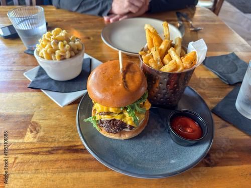 Canvas-taulu Gourmet burger, fries, and mac and cheese on a wooden table.