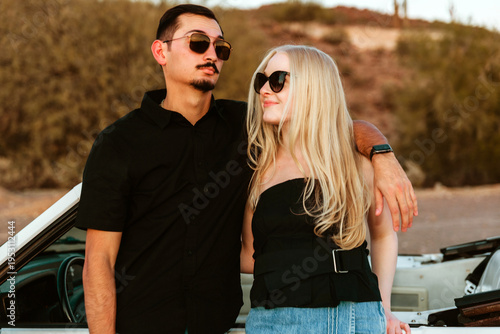 young couple standing in desert with convertible