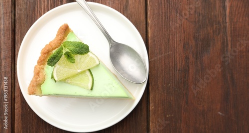 Piece of delicious lime pie with mint and spoon on wooden table, top view. Space for text