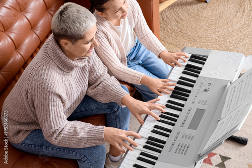 Female music teacher giving synthesizer lesson to little girl at home, top view