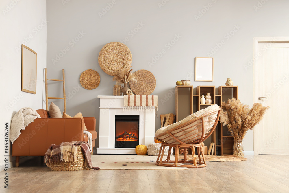 Obraz premium Interior of living room with leather sofa, armchair, shelving unit, wicker basket, fireplace and autumn decorations