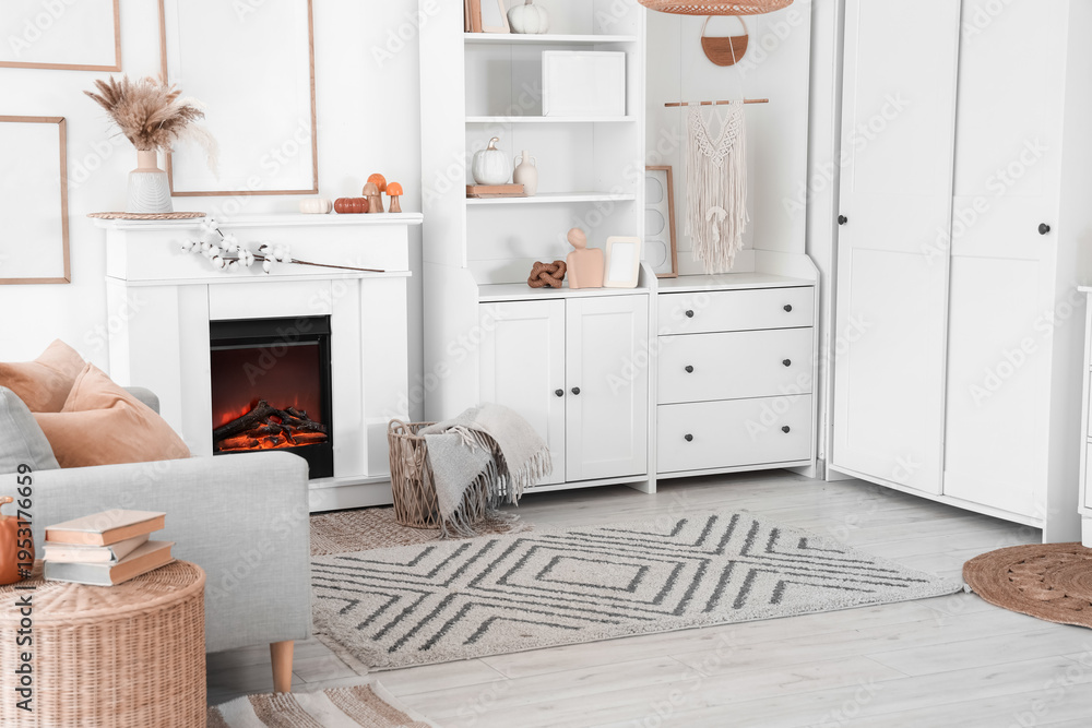 Naklejka premium Interior of living room with grey sofa, coffee table, shelving units and autumn home decor on fireplace near white wall