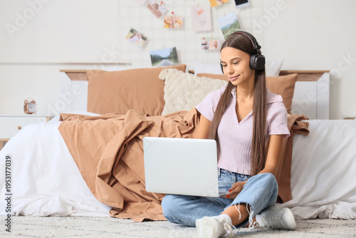 Teenage girl with headphones using laptop in bedroom