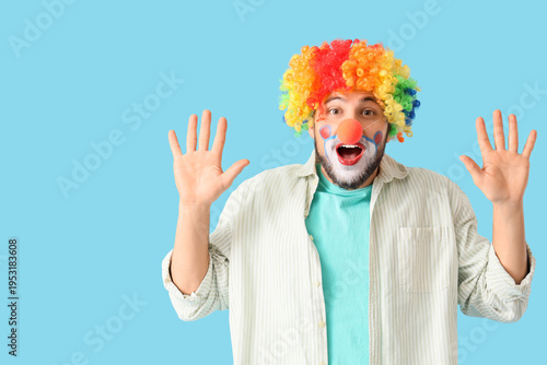 Shocked young man in clown disguise on blue background