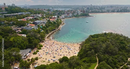 Shelly Beach in Manly, Sydney: vibrant summer scene with many people relaxing on the sand, swimming in the clear blue ocean, and enjoying the coastal atmosphere. Australia aerial view landscape