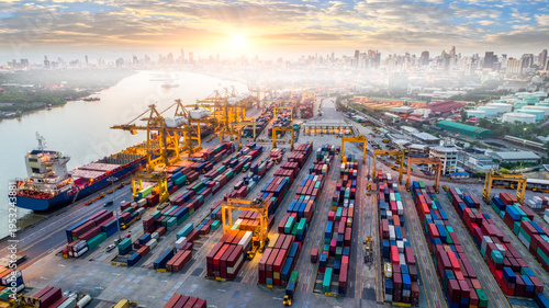 Aerial view and top view Logistics and transportation of Container Cargo ship and Cargo plane with working crane bridge in shipyard at sunrise, logistic import export and transport industry background