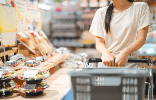 Young adult asian woman consumer choosing ready meals cooked food at supermarket store choice buying