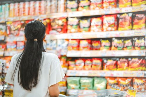Rear view young adult asian woman customer choosing snack food from shelf shopping at asia supermarket