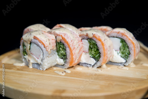 Sushi roll with salmon, cheese and avocado. Maki roll with shrimps fried, avocado and lattuce on a wooden plate . Delicious sushi rolls served on grey table