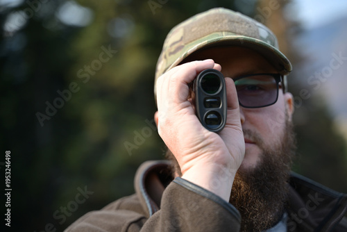 Photography Bearded man using a rangefinder while hunting in the outdoors with camouflage ca
