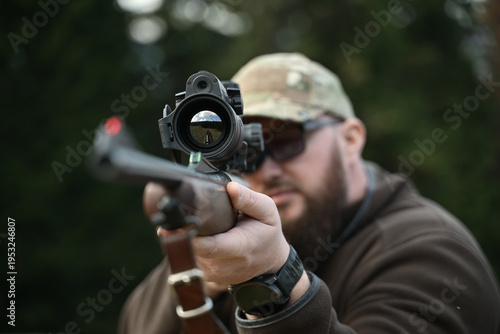 Tableau sur toile Hunter aiming a scoped rifle downrange during outdoor target practice in camoufl