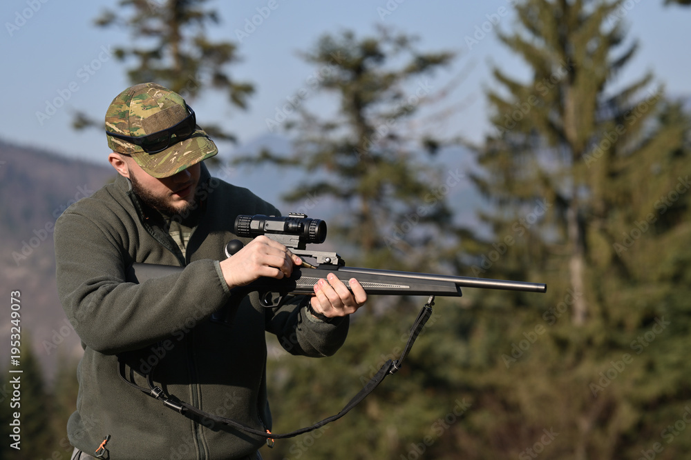 Fototapeta premium Hunter adjusting rifle scope while preparing for hunting in forested mountain landscape