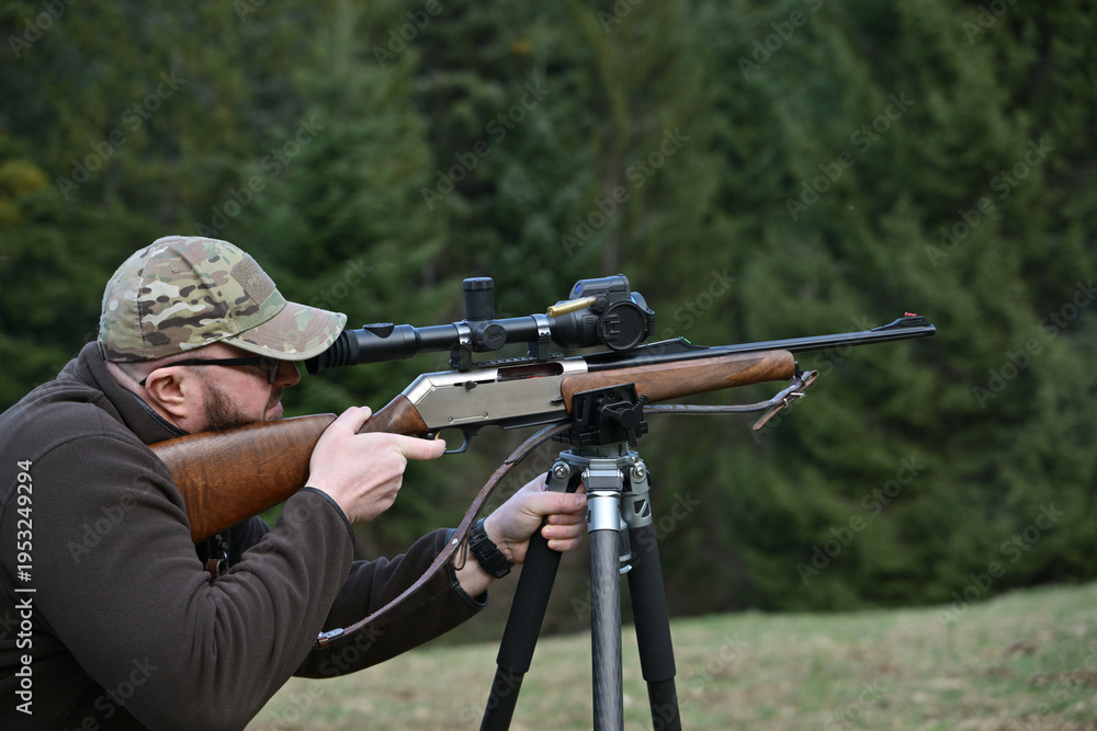 Fototapeta premium Hunter aiming a scoped rifle from a tripod in a forest clearing during outdoor hunting practice