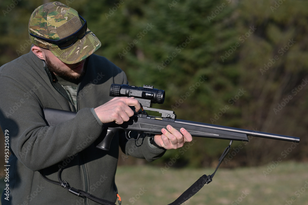 Fototapeta premium Hunter adjusting scope on a bolt-action rifle at a woodland shooting range during daytime