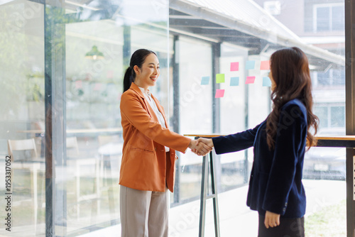 Photos A scene depicting two women in blazers engaging in a friendly handshake in a well-lit office, illustrating the importance of greeting and goodwill in business interactions
