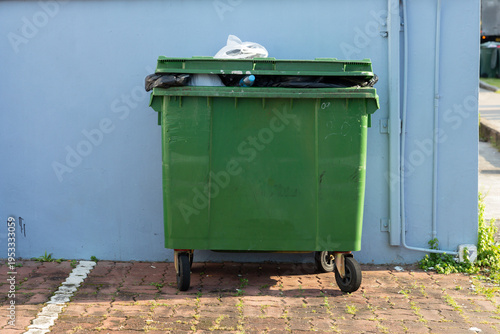 Garbage bin with overflowing bag next to blue wall