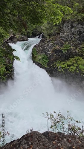 Vertical close up of a powerful mountain waterfall cascading over dark rocks.