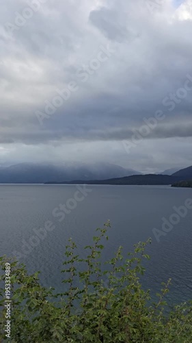 Vertical landscape of a calm mountain lake and dark forest on a moody cloudy day.