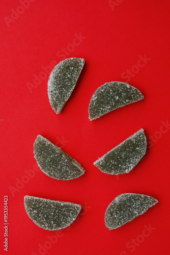 Dark gummy candies shaped like slices sit on red background