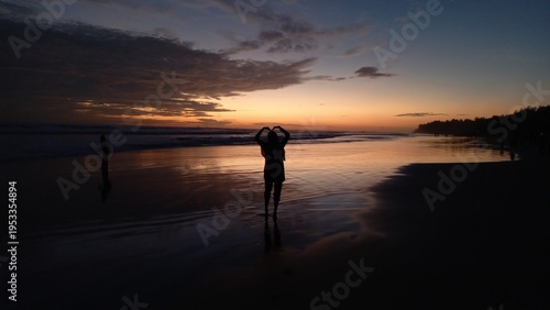 Silhouette of a female tourist playing on the beach at sunset