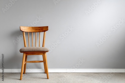 Wooden chair with a padded seat against a gray wall.
