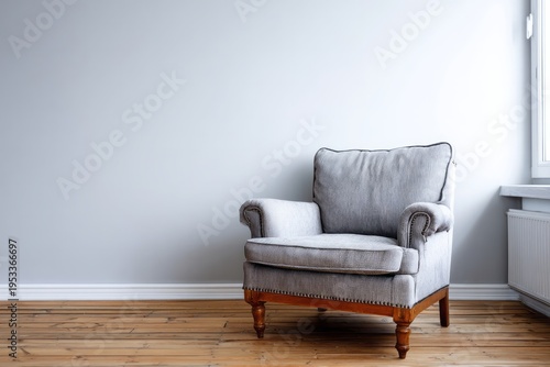A comfortable armchair sits against a plain wall with wooden flooring.