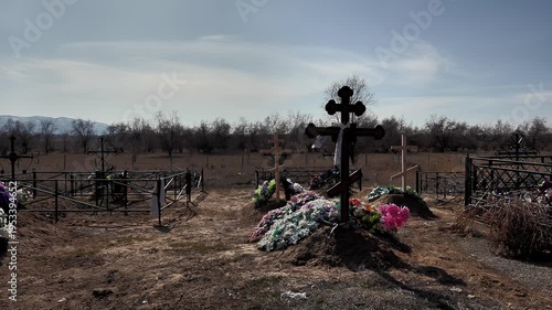 the wind ruffles a memorial scarf on the cross and dry autumn grass in an old rural cemetery, general plan