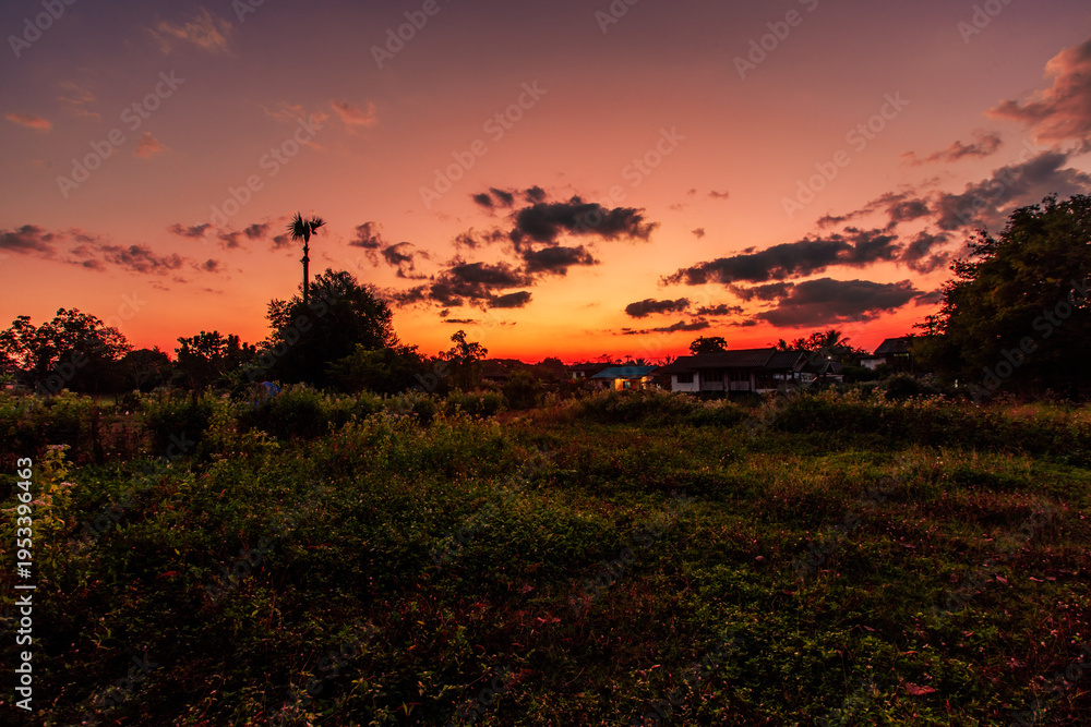 Fototapeta premium A natural backdrop of twilight sky and beautiful changing sunsets during a trip to Thailand, featuring mountains, rice fields, and temporary huts.