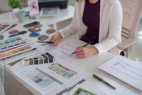 Asian adult designer draws floor plans selects color palettes for home office project creating architectural layout in bright modern studio