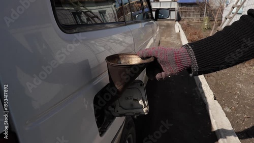 A man pours fuel into a car through the neck using a canister