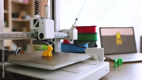 A 3D printer meticulously builds a small yellow figurine layer by layer on its heated print bed