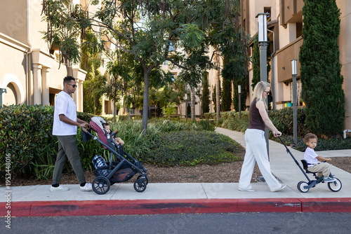 a mixed race young family going for a walk with a stroller and a mini bicycle