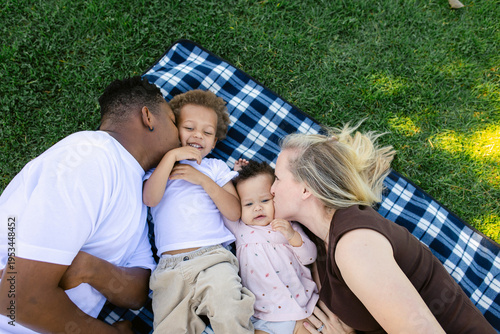 A young family at the park laying on a picnic blanket, being playful and laughing