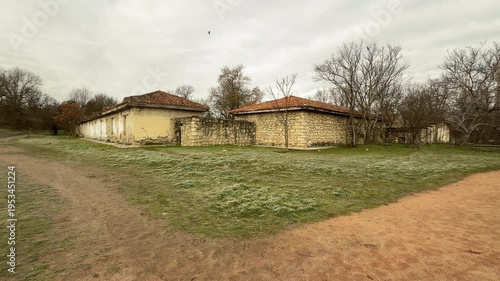 Wallpaper Mural Rustic walking trails curve around old stone houses on a chilly, overcast day. The weathered walls and red tiled roofs create a lonely, historic feeling in the quiet park. Bare trees stand tall. Torontodigital.ca