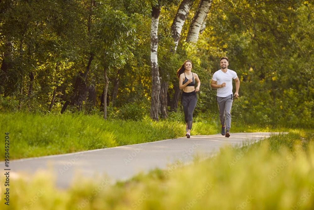 Obraz premium Morning healthy run of happy couple in summer park, fit man and woman training outdoors. Friends athletes or husband and wife running together to enjoy nature and time together. Workout, life concept